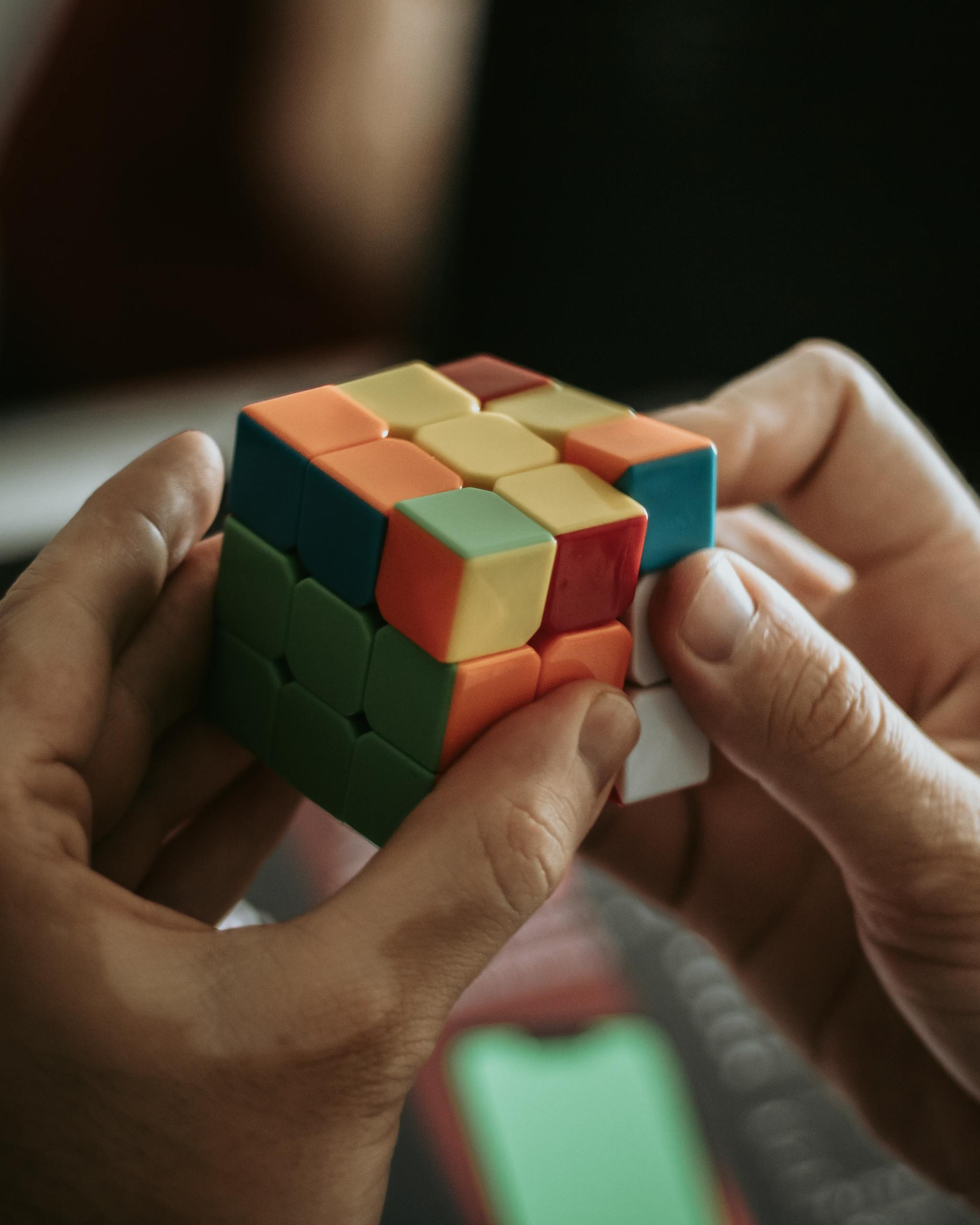 Close-up of hands solving a colorful Rubik's cube indoors.